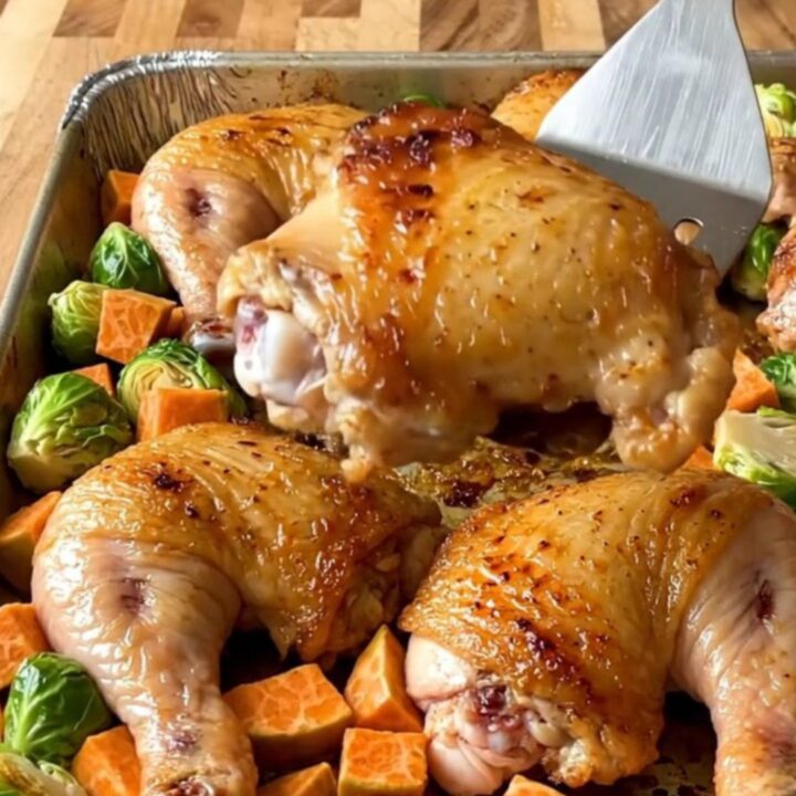 A sheet pan filled with golden-brown roasted chicken thighs, halved Brussels sprouts, and roasted sweet potato cubes.