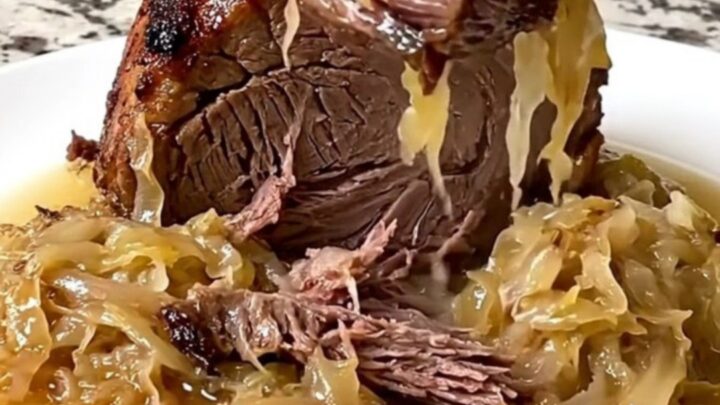 A rustic, slow-cooked beef chuck roast topped with tangy sauerkraut and onions in a black slow cooker insert.