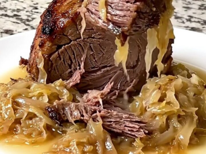 A rustic, slow-cooked beef chuck roast topped with tangy sauerkraut and onions in a black slow cooker insert.