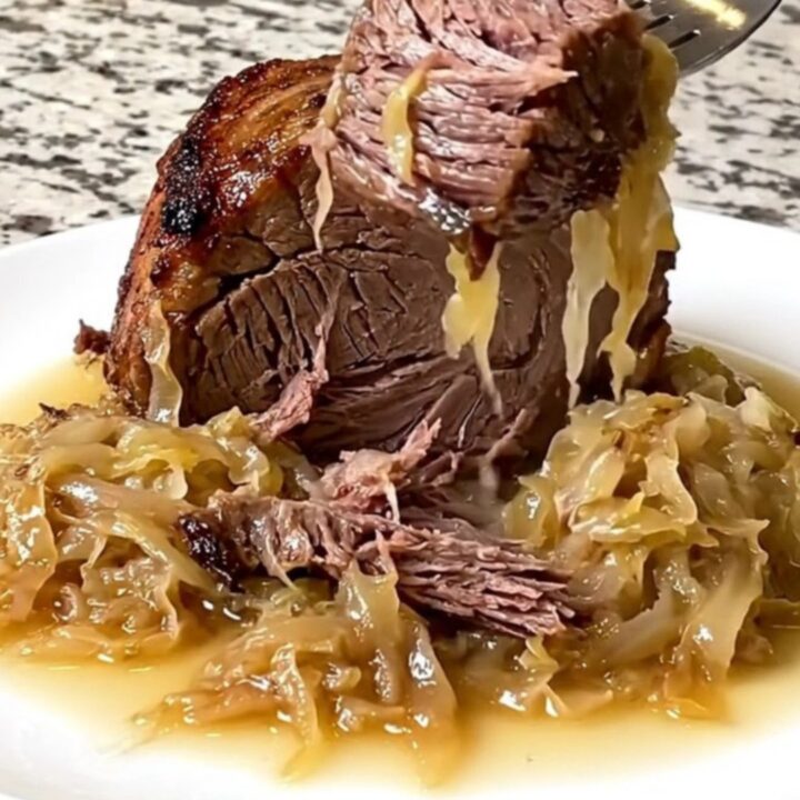 A rustic, slow-cooked beef chuck roast topped with tangy sauerkraut and onions in a black slow cooker insert.