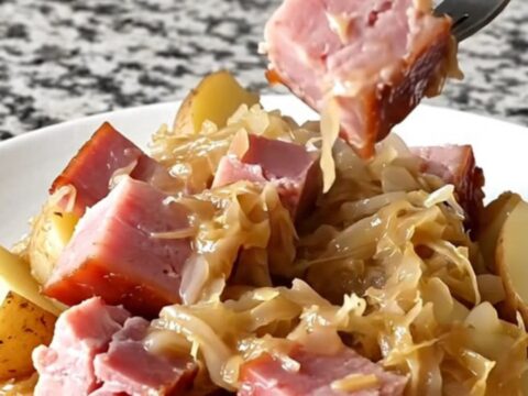 Close-up of tender smoked ham, sauerkraut, and potatoes in a black slow cooker insert.