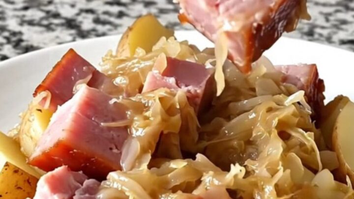 Close-up of tender smoked ham, sauerkraut, and potatoes in a black slow cooker insert.