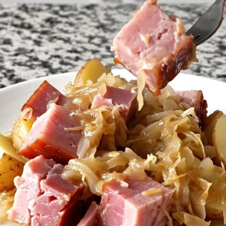 Close-up of tender smoked ham, sauerkraut, and potatoes in a black slow cooker insert.