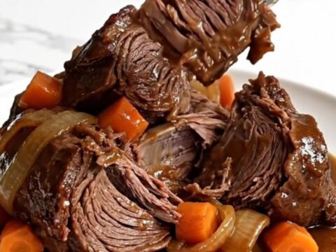 A whole raw beef chuck roast in a slow cooker with carrots and onions.
