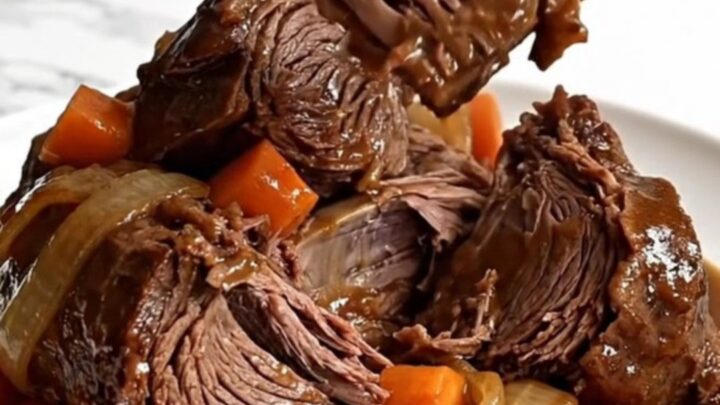 A whole raw beef chuck roast in a slow cooker with carrots and onions.
