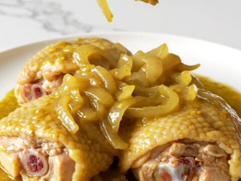 A close-up of tender, slow-cooked bone-in chicken thighs covered in a rich, golden mustard sauce with soft onions.