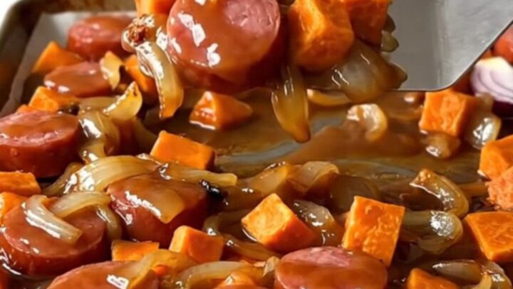 A sheet pan filled with roasted kielbasa, sweet potato cubes, and red onions with a golden brown sugar glaze.