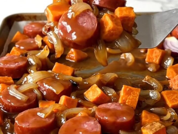 A sheet pan filled with roasted kielbasa, sweet potato cubes, and red onions with a golden brown sugar glaze.