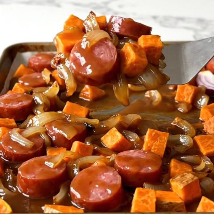 A sheet pan filled with roasted kielbasa, sweet potato cubes, and red onions with a golden brown sugar glaze.