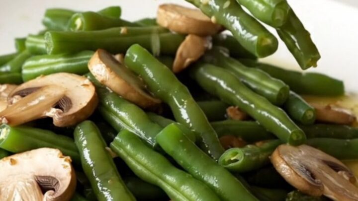A high-angle shot of tender green beans and sliced mushrooms in a rich garlic butter sauce, served in a white bowl.