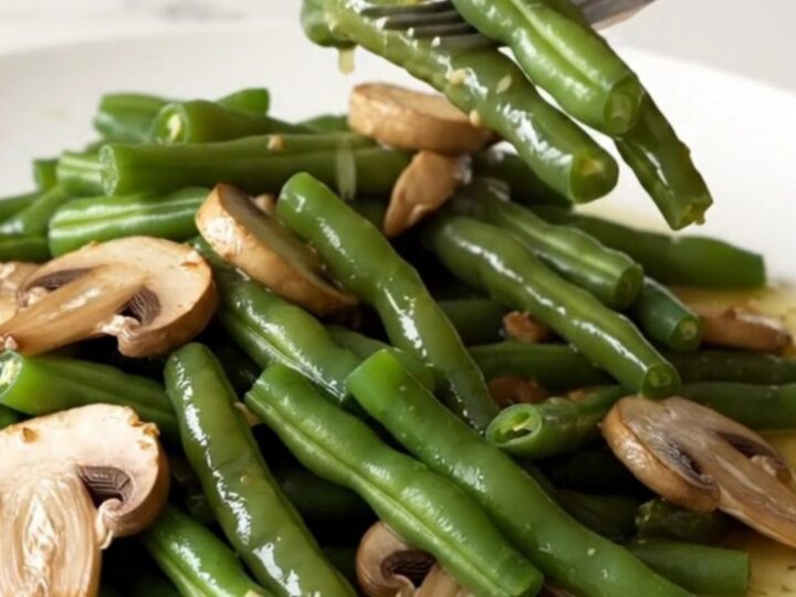 A high-angle shot of tender green beans and sliced mushrooms in a rich garlic butter sauce, served in a white bowl.
