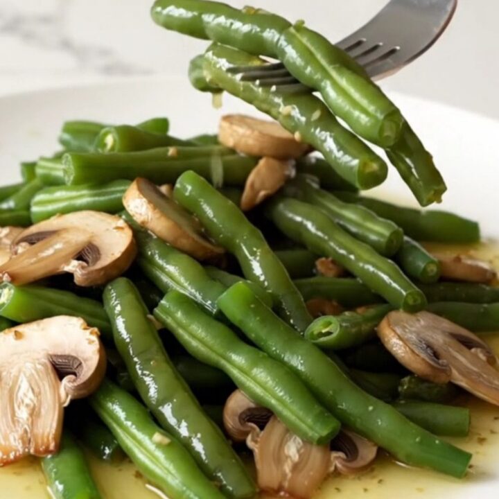 A high-angle shot of tender green beans and sliced mushrooms in a rich garlic butter sauce, served in a white bowl.