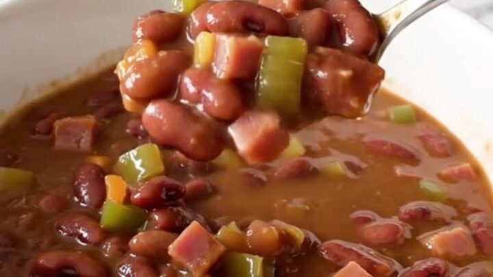A close-up of a slow cooker filled with red beans, diced ham, and vegetables in a savory broth.