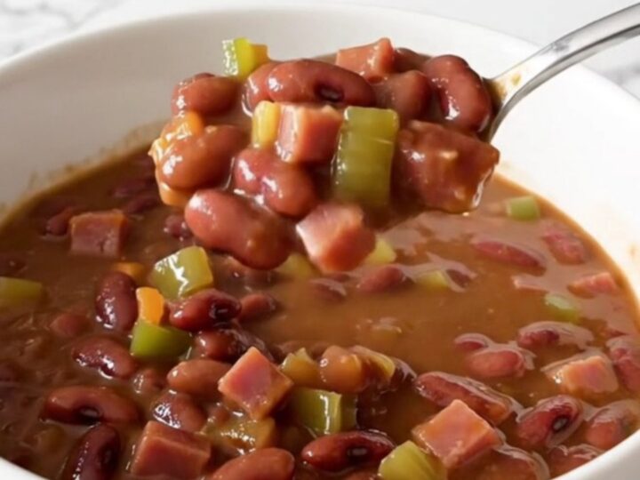 A close-up of a slow cooker filled with red beans, diced ham, and vegetables in a savory broth.