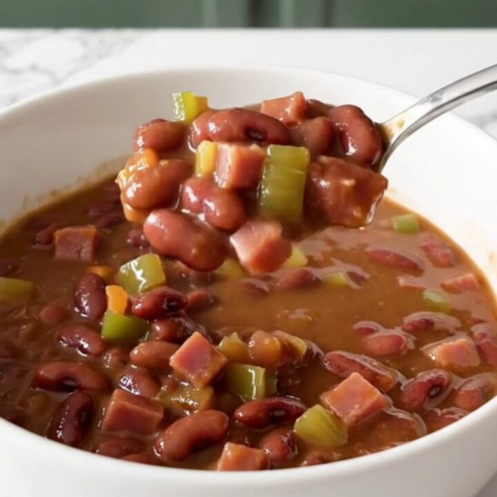 A close-up of a slow cooker filled with red beans, diced ham, and vegetables in a savory broth.