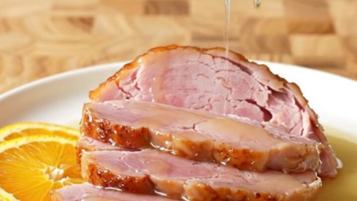 A large, succulent bone-in ham in a slow cooker topped with orange slices and a honey glaze.