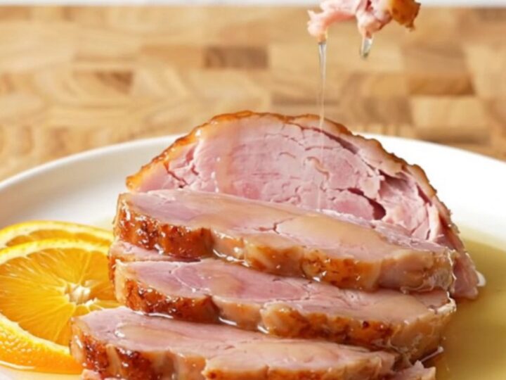 A large, succulent bone-in ham in a slow cooker topped with orange slices and a honey glaze.