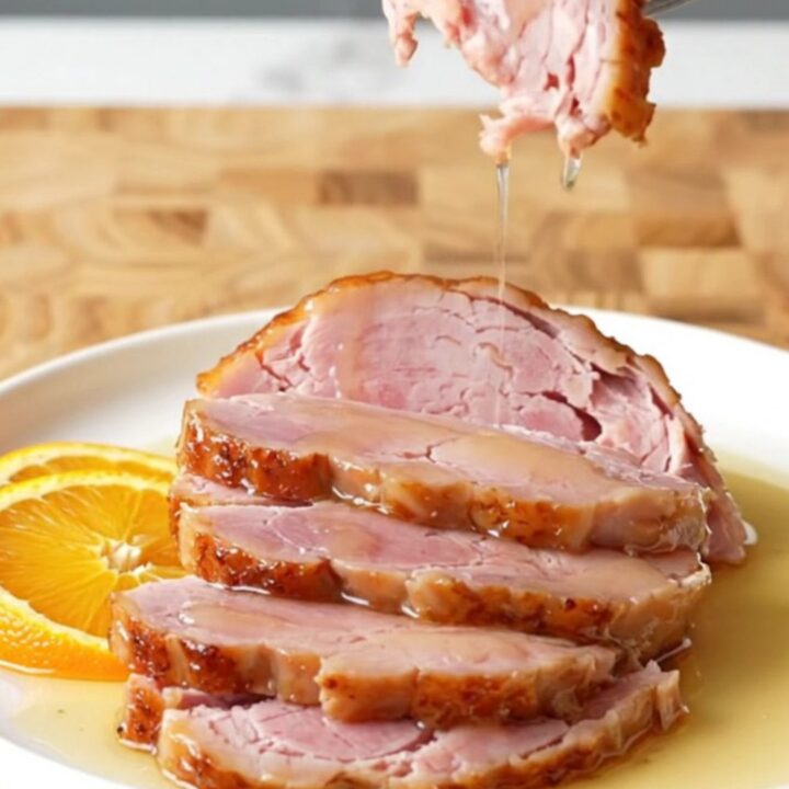 A large, succulent bone-in ham in a slow cooker topped with orange slices and a honey glaze.