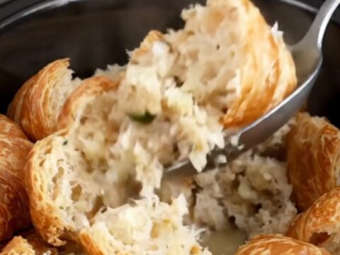 A close-up of slow cooker croissant stuffing with fresh herbs in a black stoneware insert.