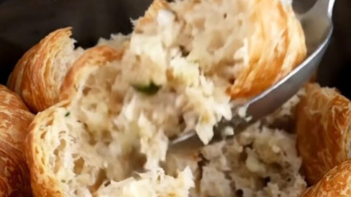 A close-up of slow cooker croissant stuffing with fresh herbs in a black stoneware insert.