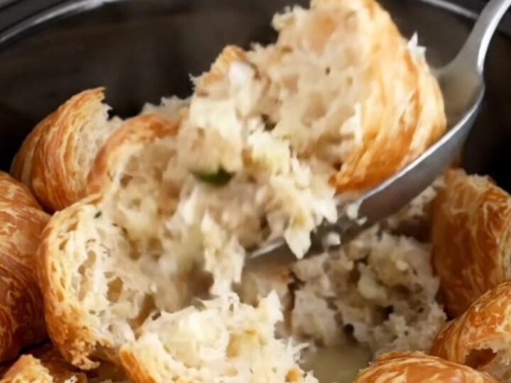 A close-up of slow cooker croissant stuffing with fresh herbs in a black stoneware insert.