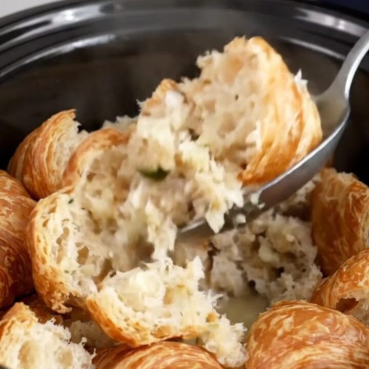 A close-up of slow cooker croissant stuffing with fresh herbs in a black stoneware insert.