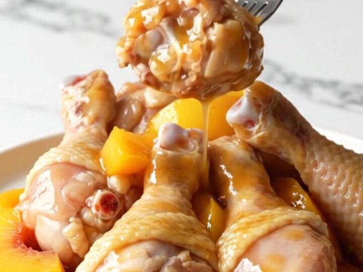 Slow cooker peach bourbon chicken drumettes served on a white plate with visible peach slices and thick amber sauce.