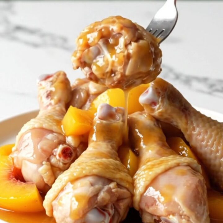 Slow cooker peach bourbon chicken drumettes served on a white plate with visible peach slices and thick amber sauce.