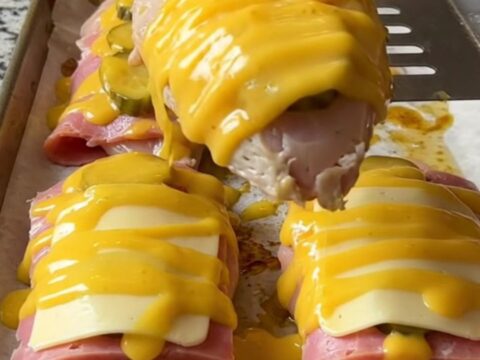 A sheet pan filled with golden-baked chicken breasts topped with ham, pickles, and melted Swiss cheese.