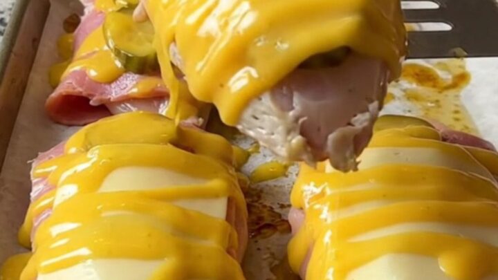 A sheet pan filled with golden-baked chicken breasts topped with ham, pickles, and melted Swiss cheese.