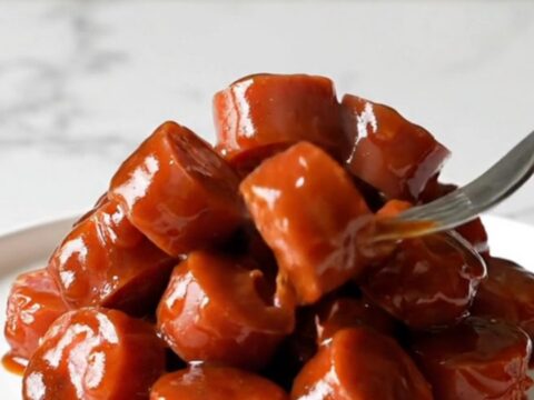 A close-up of Korean BBQ kielbasa bites in a slow cooker, glazed in a dark, rich sauce with visible onions and sesame seeds.