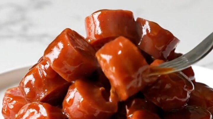 A close-up of Korean BBQ kielbasa bites in a slow cooker, glazed in a dark, rich sauce with visible onions and sesame seeds.