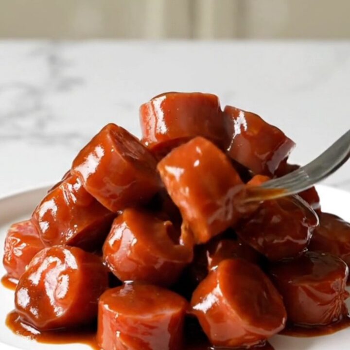 A close-up of Korean BBQ kielbasa bites in a slow cooker, glazed in a dark, rich sauce with visible onions and sesame seeds.