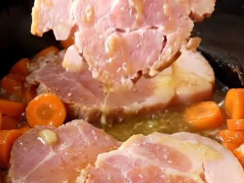 A close-up of tender ham steaks and bright orange carrot coins glazed in a buttery brown sugar sauce in a slow cooker.
