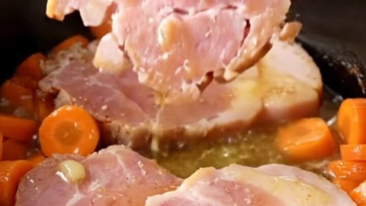 A close-up of tender ham steaks and bright orange carrot coins glazed in a buttery brown sugar sauce in a slow cooker.
