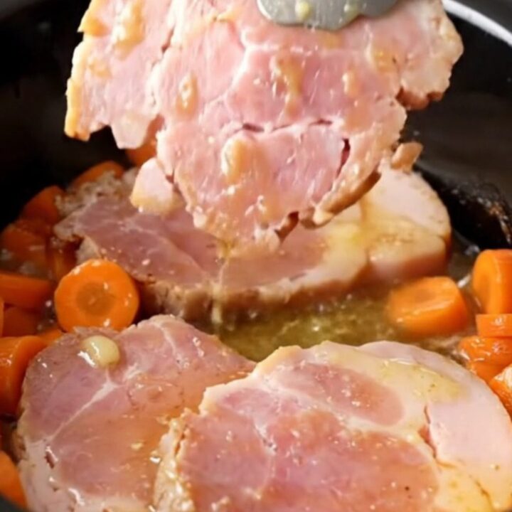 A close-up of tender ham steaks and bright orange carrot coins glazed in a buttery brown sugar sauce in a slow cooker.