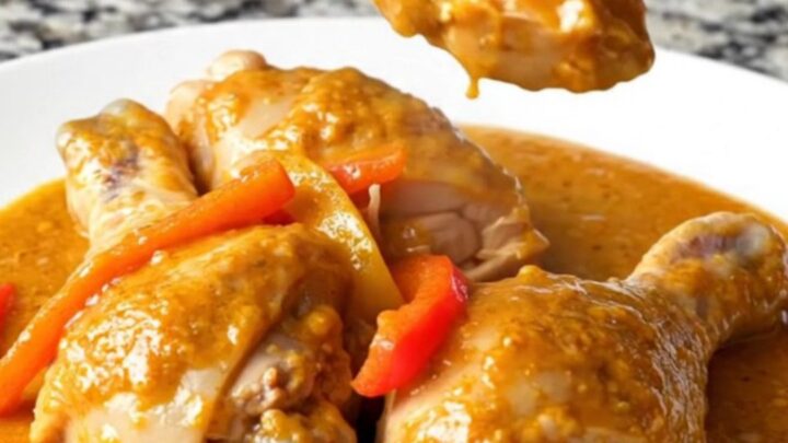 A close-up of chicken drumsticks in a rich, orange paprika sauce with pepper strips.