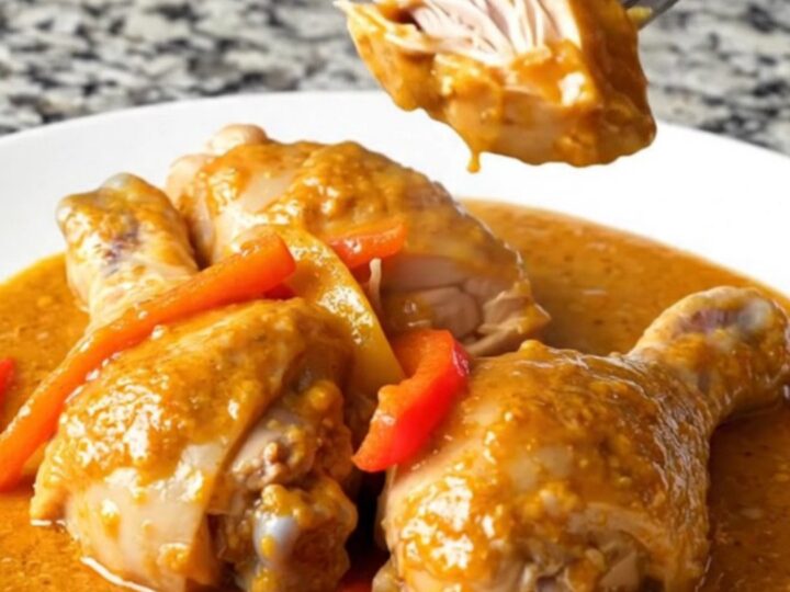 A close-up of chicken drumsticks in a rich, orange paprika sauce with pepper strips.