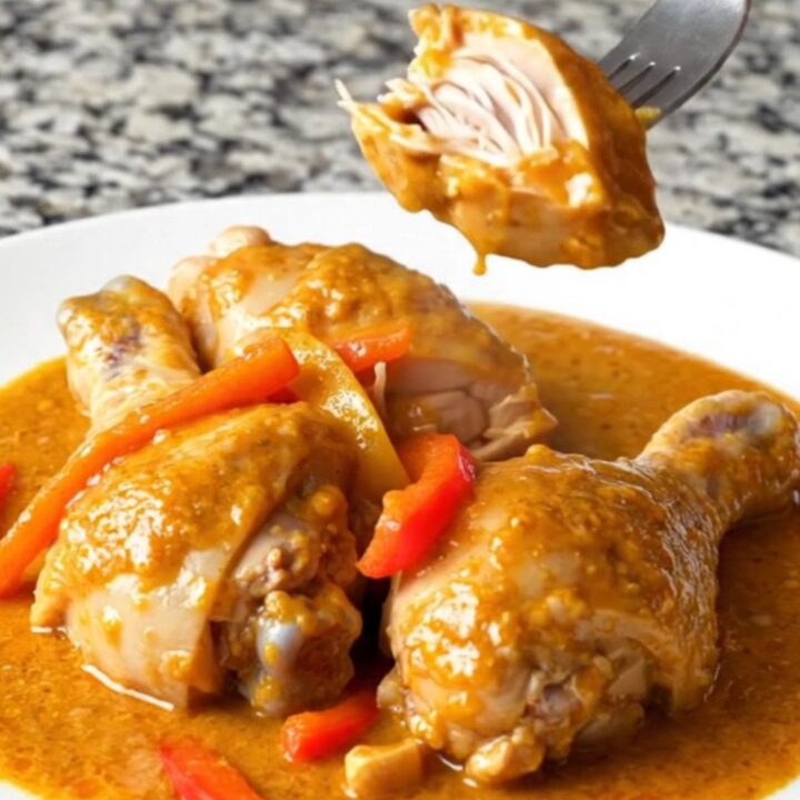 A close-up of chicken drumsticks in a rich, orange paprika sauce with pepper strips.