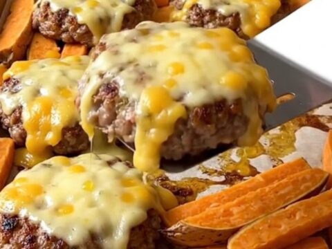 A sheet pan with cooked turkey burgers topped with melted pepper jack cheese and roasted sweet potato wedges.