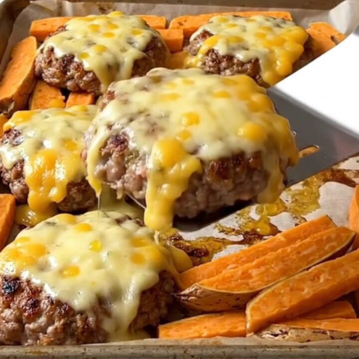 A sheet pan with cooked turkey burgers topped with melted pepper jack cheese and roasted sweet potato wedges.