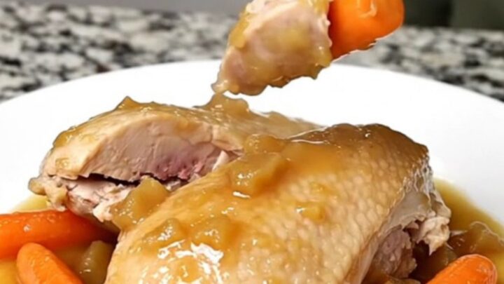 A close-up of tender, cooked chicken breasts and baby carrots in a light cider sauce on a white plate.