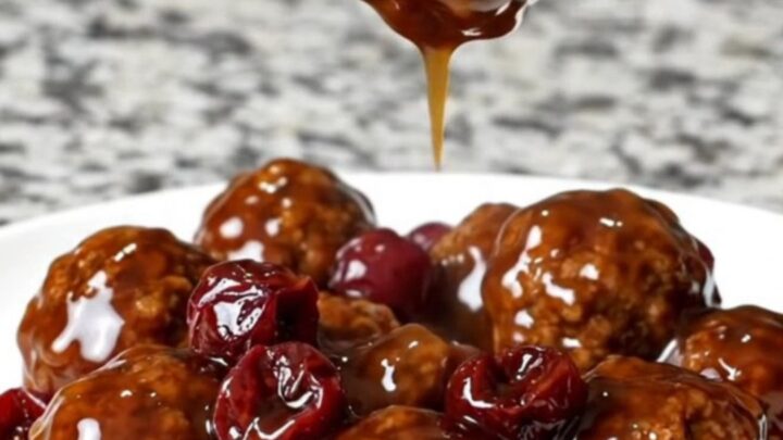 A slow cooker filled with beef meatballs coated in a dark cherry bourbon barbecue sauce.
