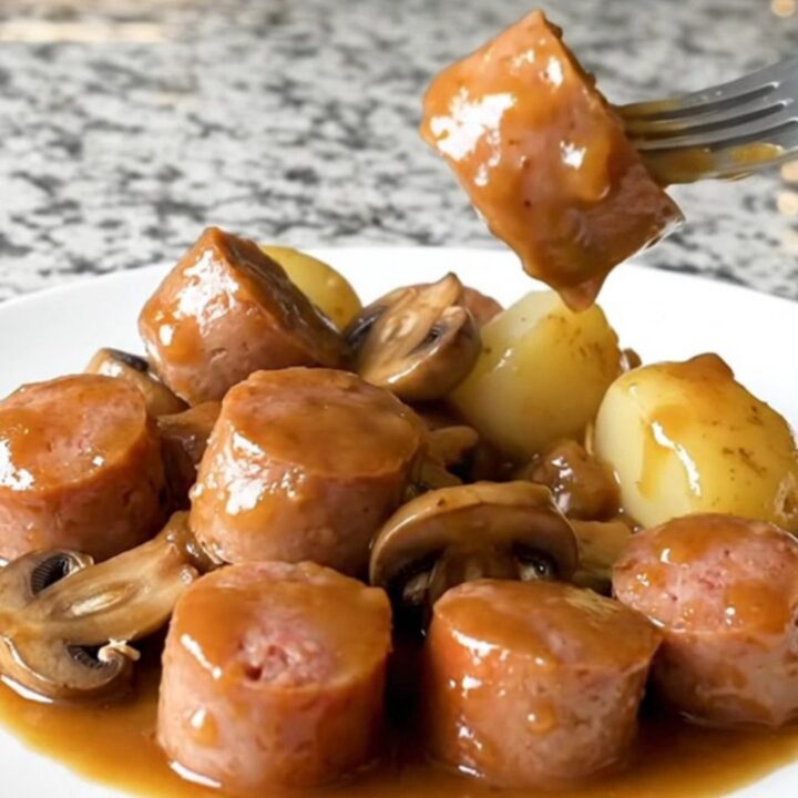 A close-up view of Italian sausage chunks, halved baby potatoes, and mushrooms in a rich Marsala sauce.