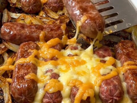 A sheet pan filled with golden-brown bratwurst, roasted baby potatoes, caramelized onion wedges, and melted cheese curds.
