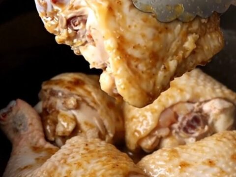 A close-up view of tender braised chicken thighs in a dark stout gravy with carrots and potatoes.