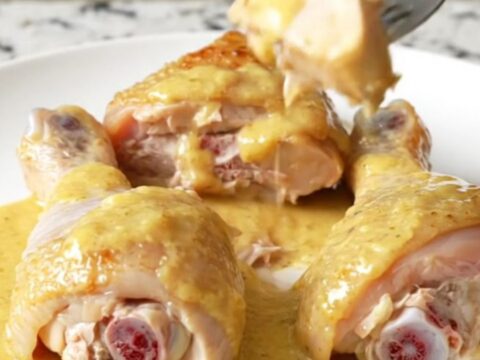 A close-up of tender chicken drumsticks and baby carrots coated in a thick, creamy honey Dijon sauce on a white plate.