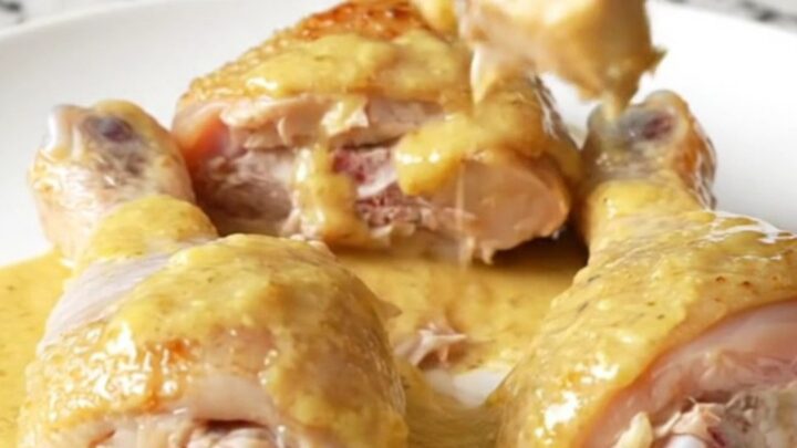 A close-up of tender chicken drumsticks and baby carrots coated in a thick, creamy honey Dijon sauce on a white plate.