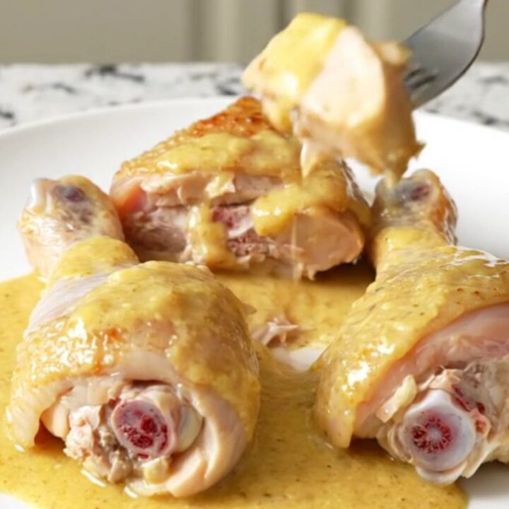 A close-up of tender chicken drumsticks and baby carrots coated in a thick, creamy honey Dijon sauce on a white plate.