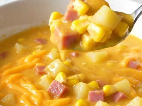 A top-down view of a creamy cheddar chowder filled with ham, corn, and potatoes in a black slow cooker insert.
